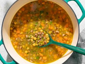 A pot of threepea soup with a ladle containing visible peas carrots and herbs