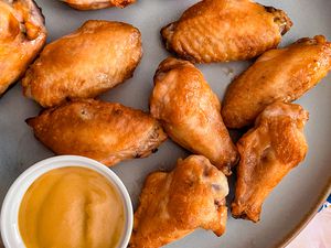 Overhead view of a gray plate of chicken wings with a small bowl of honey mustard for dipping