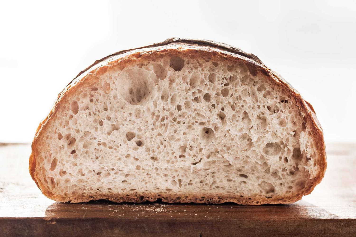 Easy kno knead bread is on a wooden cutting board and the the inside of the crusty loaf is visible.