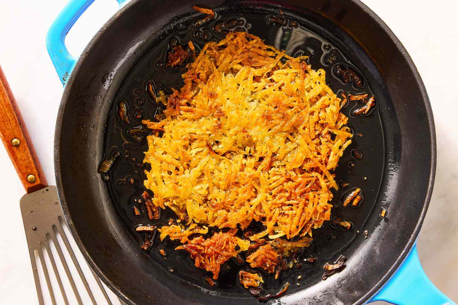 Crispy hash browns cooking in a skillet with a spatula nearby