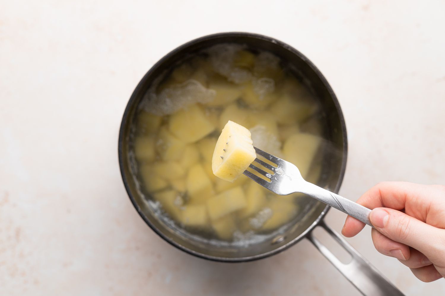 Piercing a cube of boiled potato for a garlic mashed potatoes recipe.
