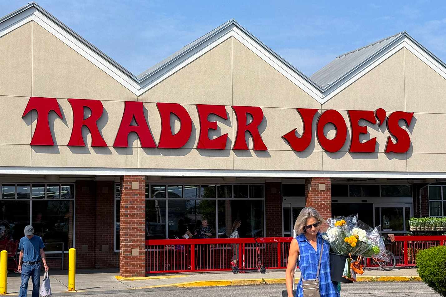 A Trader Joes storefront with a person holding flowers walking in the foreground