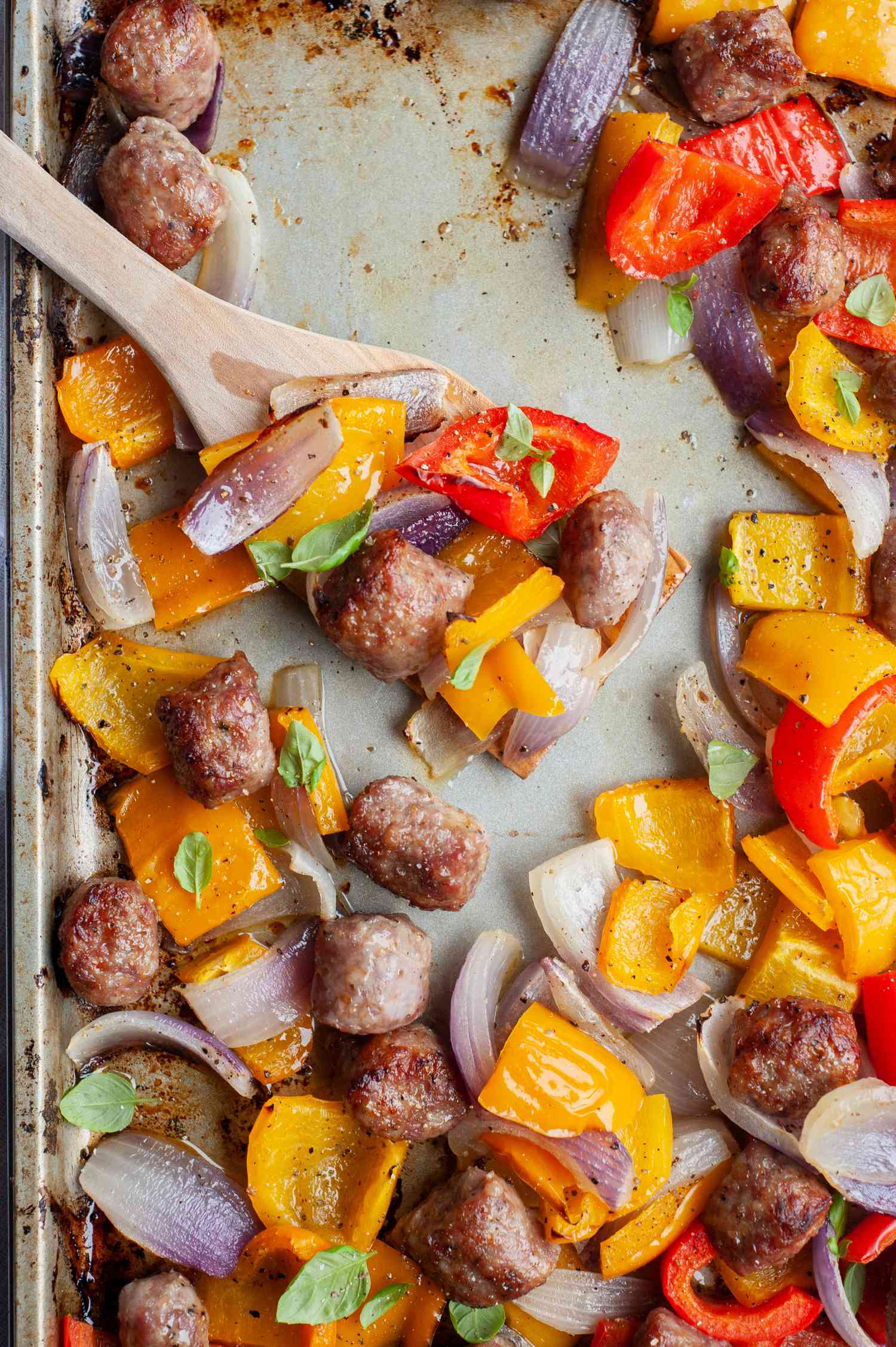 Sheet pan sausage with peppers and onions being scooped off a sheet pan.