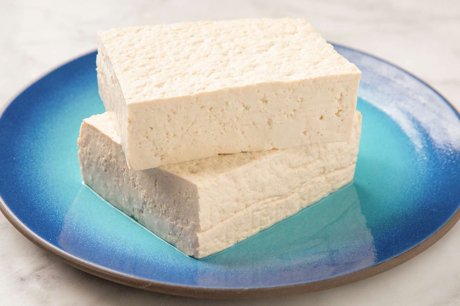 Two rectangular slices of tofu stacked on a blue ceramic plate