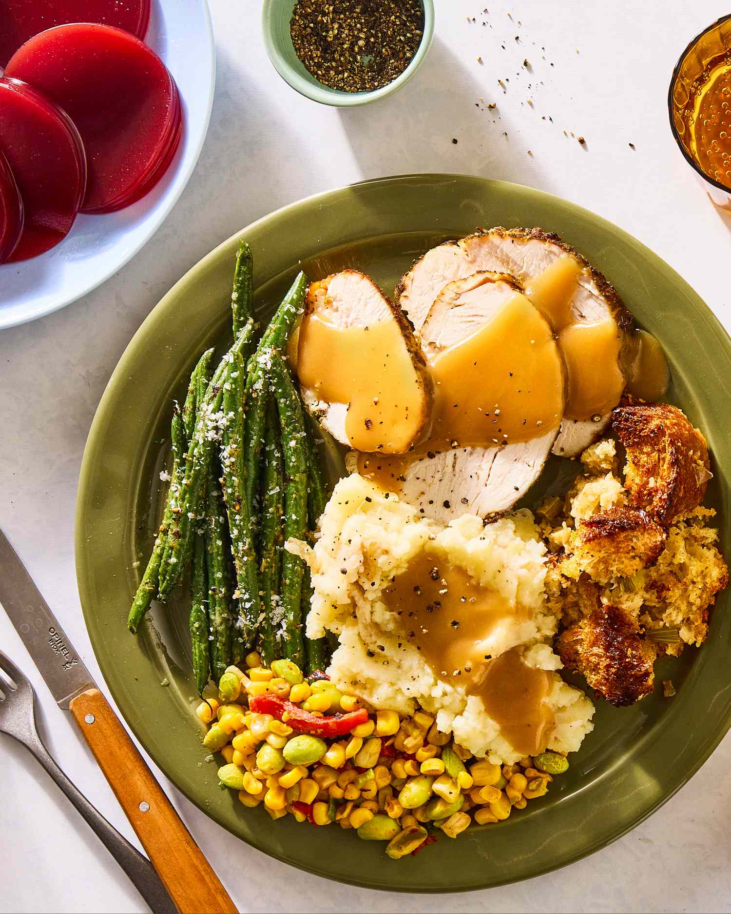 A plate with traditional Thanksgiving foods including turkey with gravy mashed potatoes stuffing green beans and corn relish