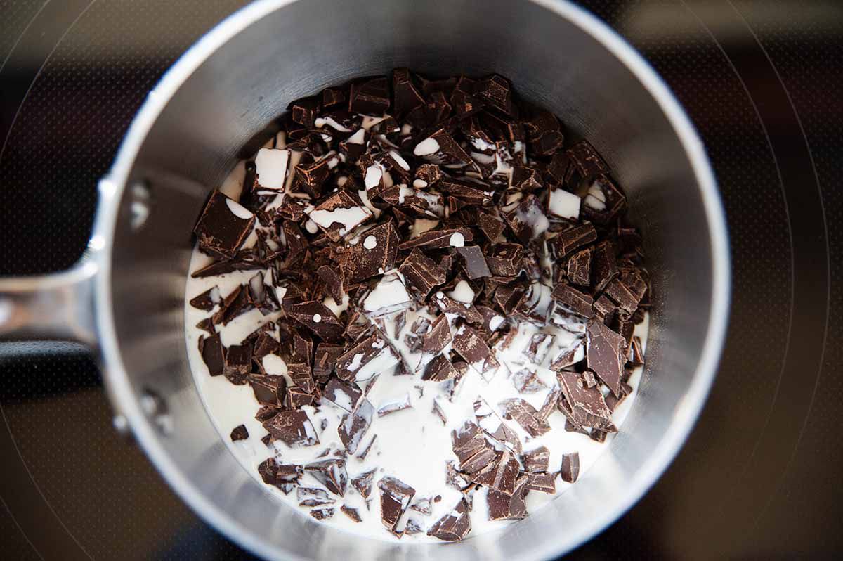 Chopped chocolate to in a pot with heavy cream to make homemade chocolate cheesecake.