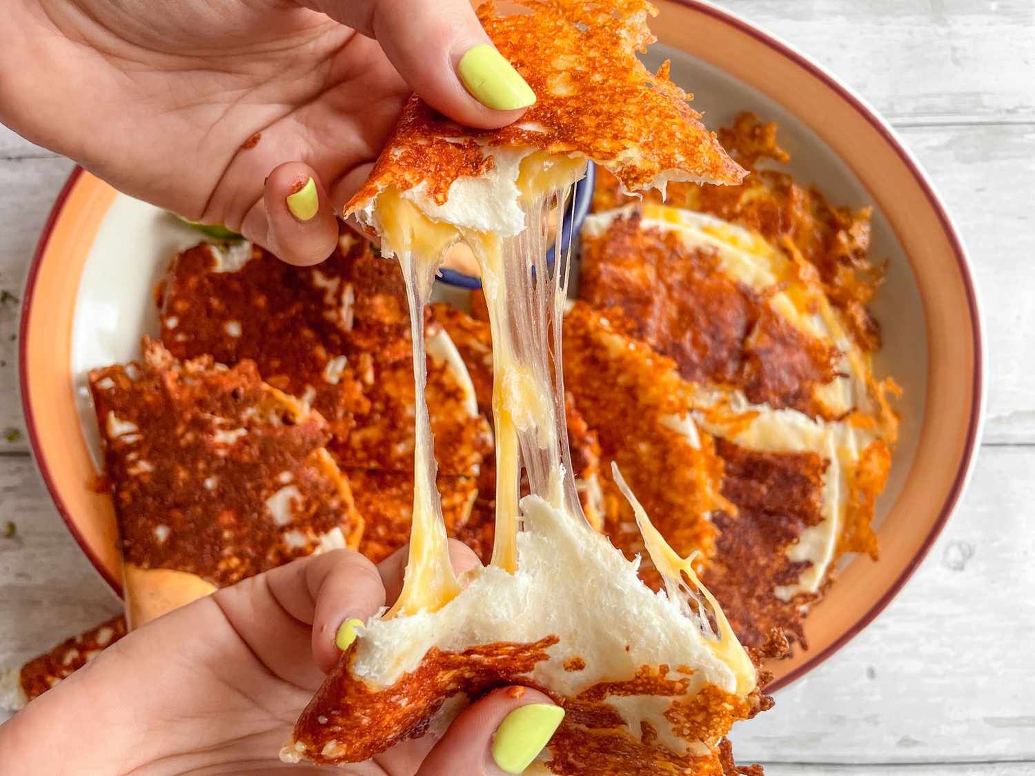 Hands Pulling Apart a Burnt Cheese Tacos to Show Cheese Pull