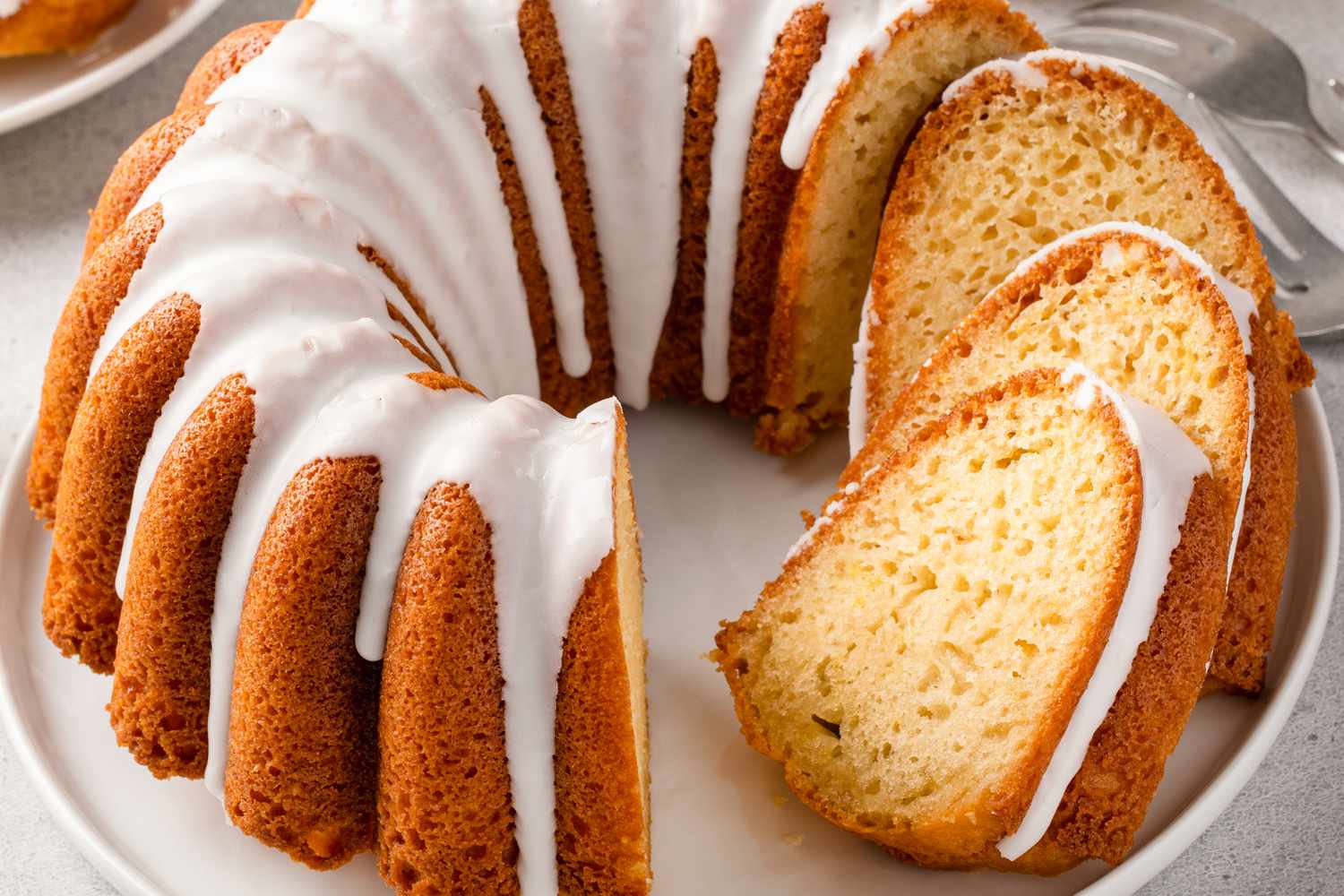 Vanilla bundt cake with white icing dripping down the sides and a few slices cut and shingled to show the crumb
