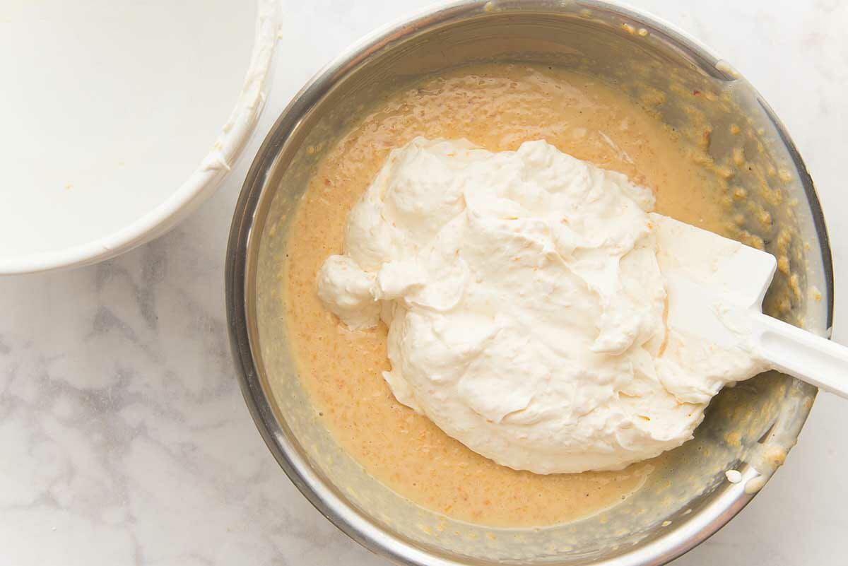 A metal bowl with whipped cream being mixed into peach puree to show how to make easy no-churn ice cream.