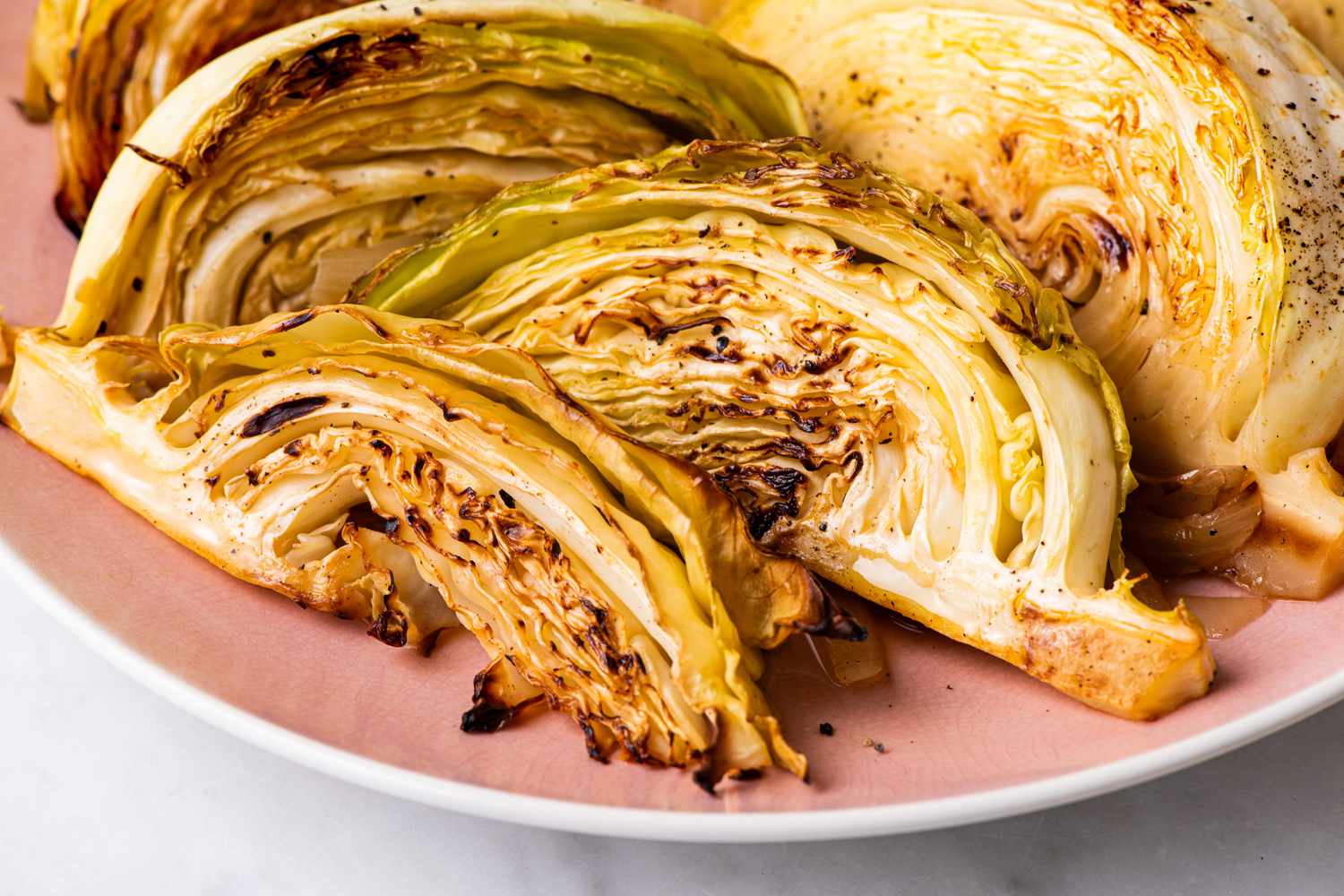 Angled view of wedges of melting cabbage on a pink plate