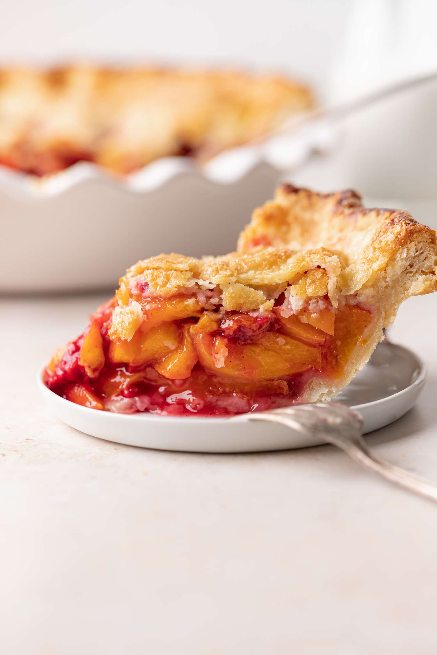 Side view of a slice of easy peach raspberry pie with the whole pie set behind it.
