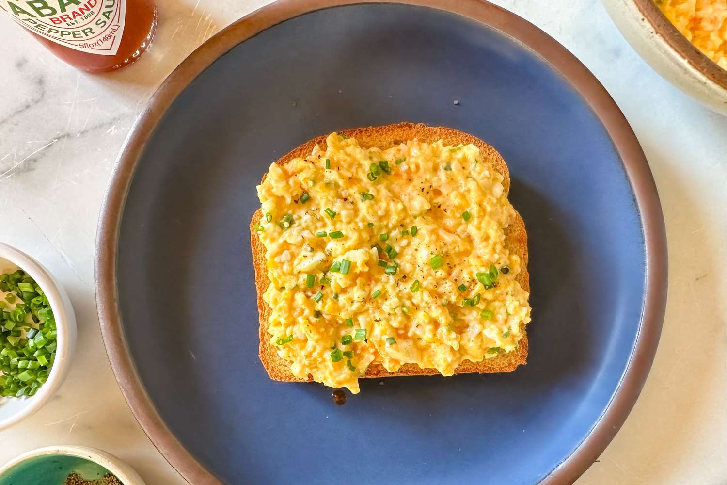 a plate with toast topped with The 5-Ingredient Egg Salad Served at Royal Tea, various ingredients on the side