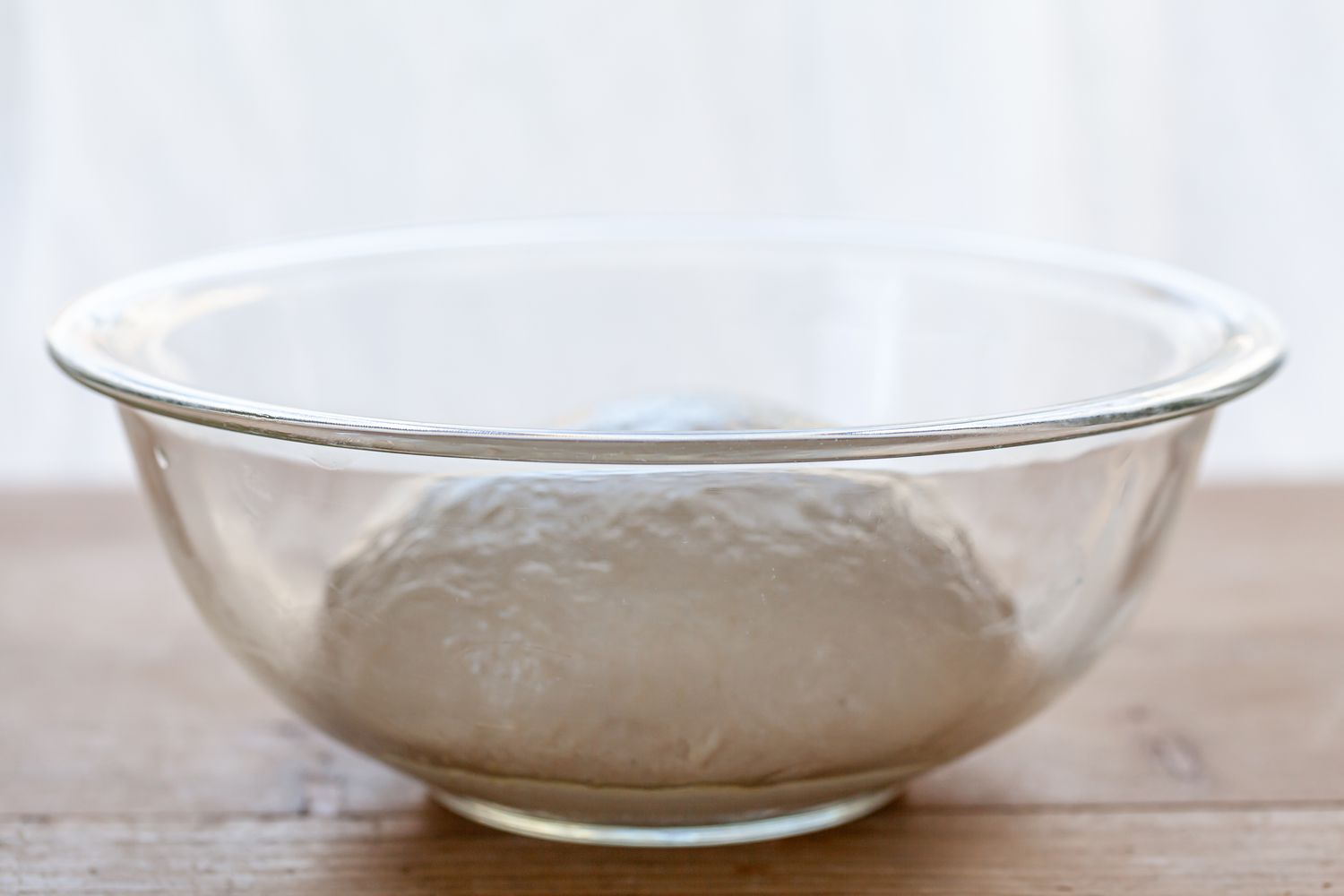 Pizza dough in a glass bowl.