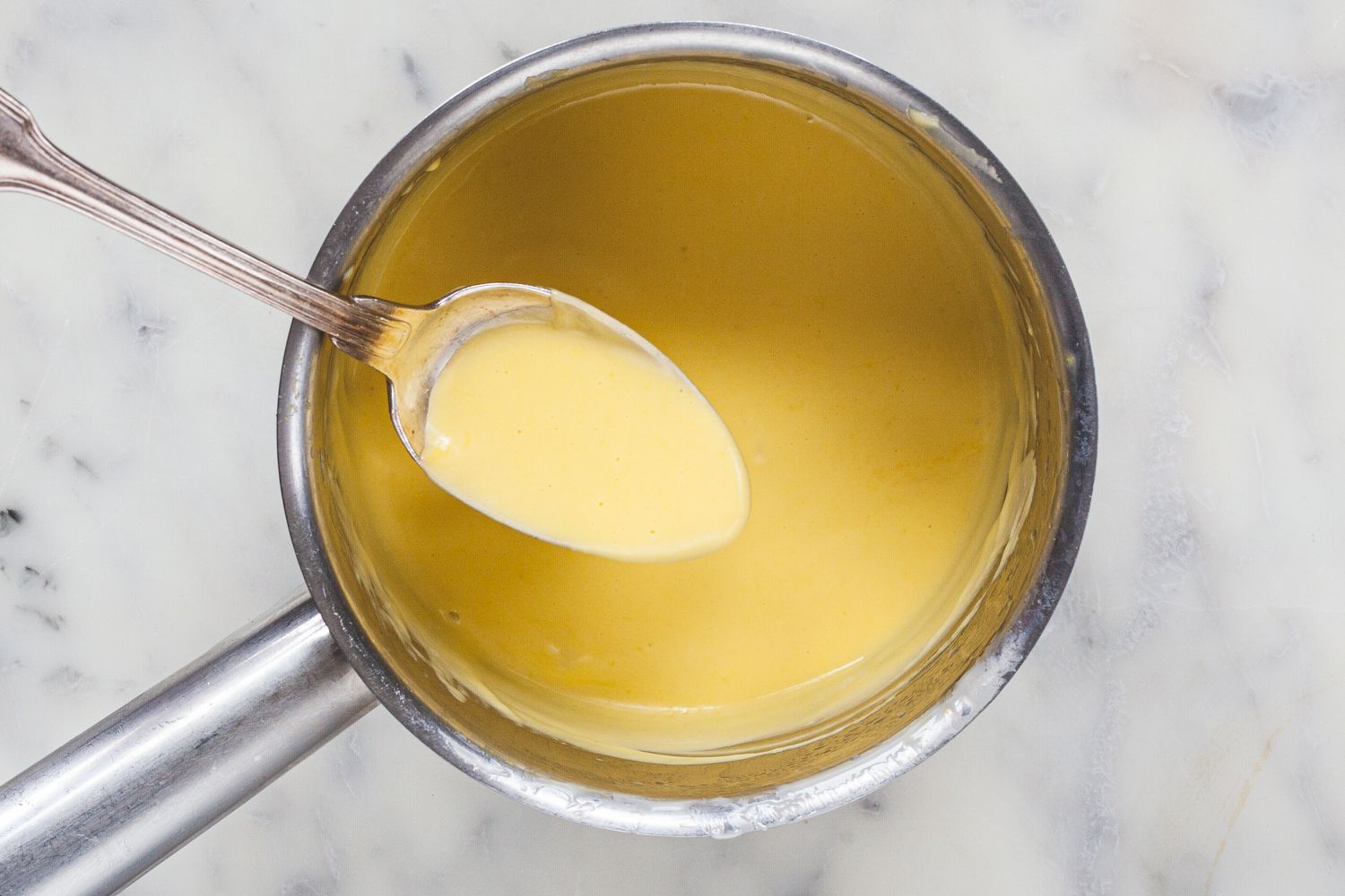 Spooning sauce out of a sauce pan to show How to Make Hollandaise for Eggs Benedict.