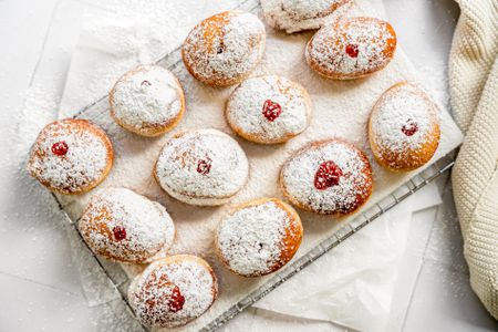 Sufganiyot (Israeli Jelly Donuts) on a Lined Cooling Rack Sitting on Parchment Paper and Next to a Knit Fabric 