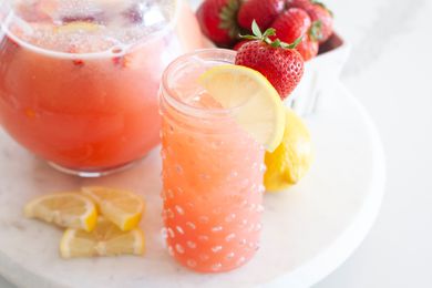 Blender strawberry lemonade served in a glass and in a pitcher with lemon slices and strawberries set around it.