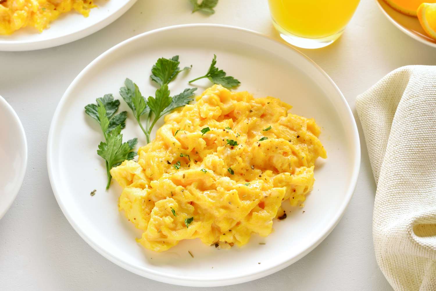A white plate with scrambled eggs, garnished with fresh parsley and chives