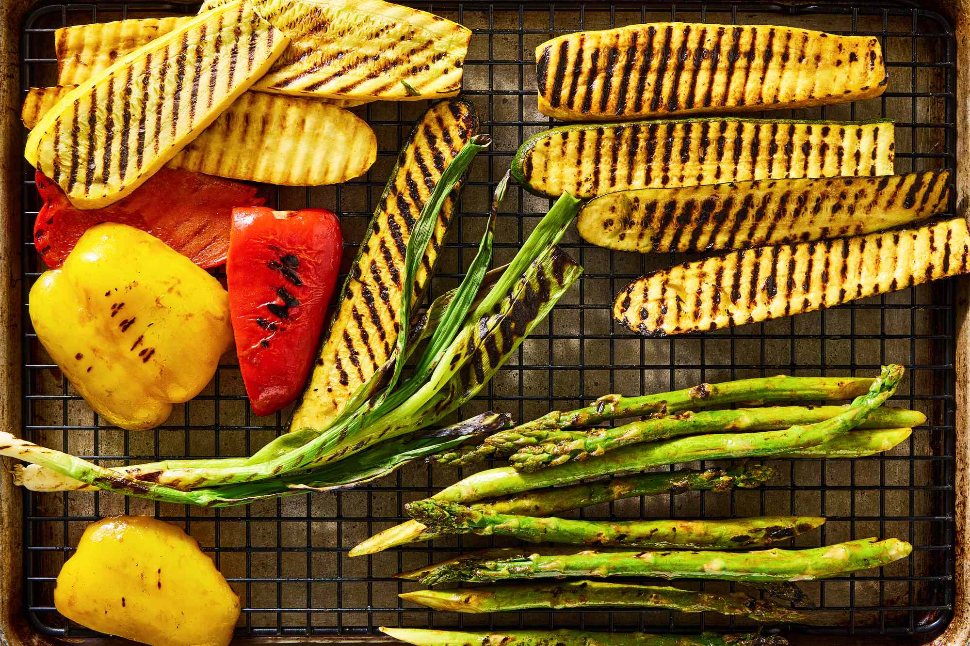 Grilled vegetables including bell peppers, zucchini, squash, and asparagus arranged on a cooling rack