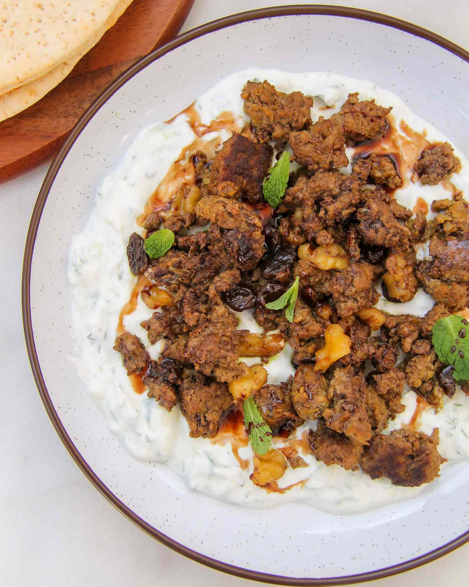 Dish of seasoned ground meat over yogurt on a plate served with bread on the side