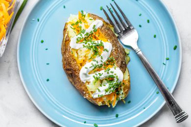 Microwave Baked Potato Topped with Sour Cream, Cheddar, and Chives on a Plate with a Fork