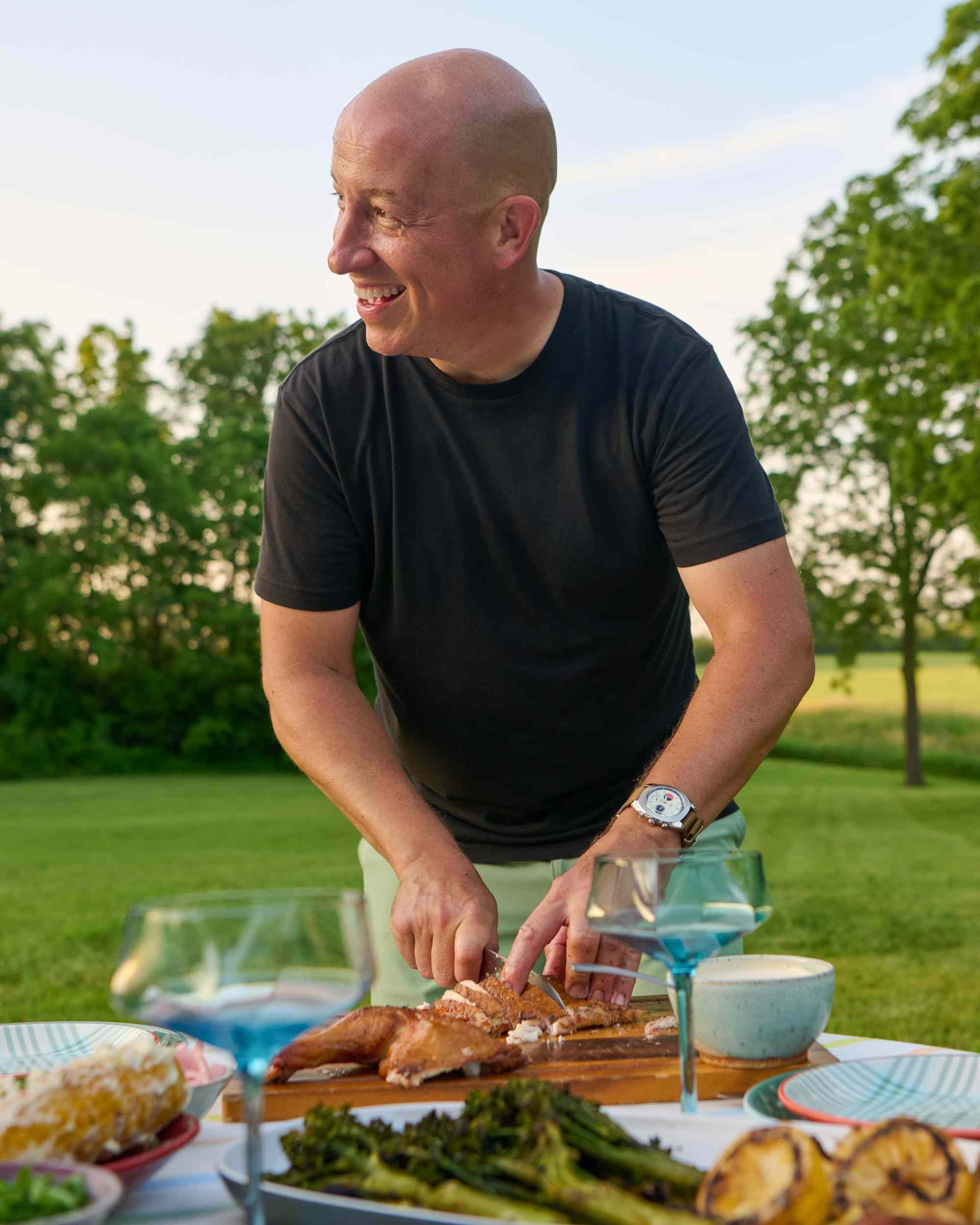 Mike Lang cutting food outdoors on a table with various plates and glasses
