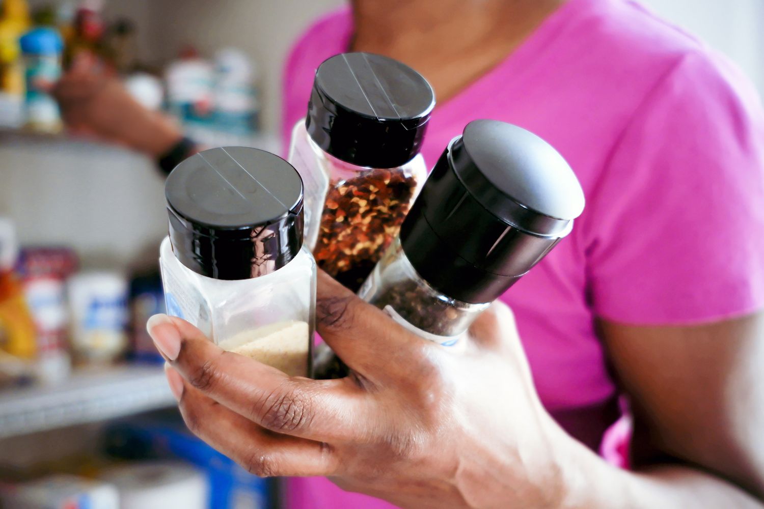 A person holding three spice jars in their hand standing near a pantry