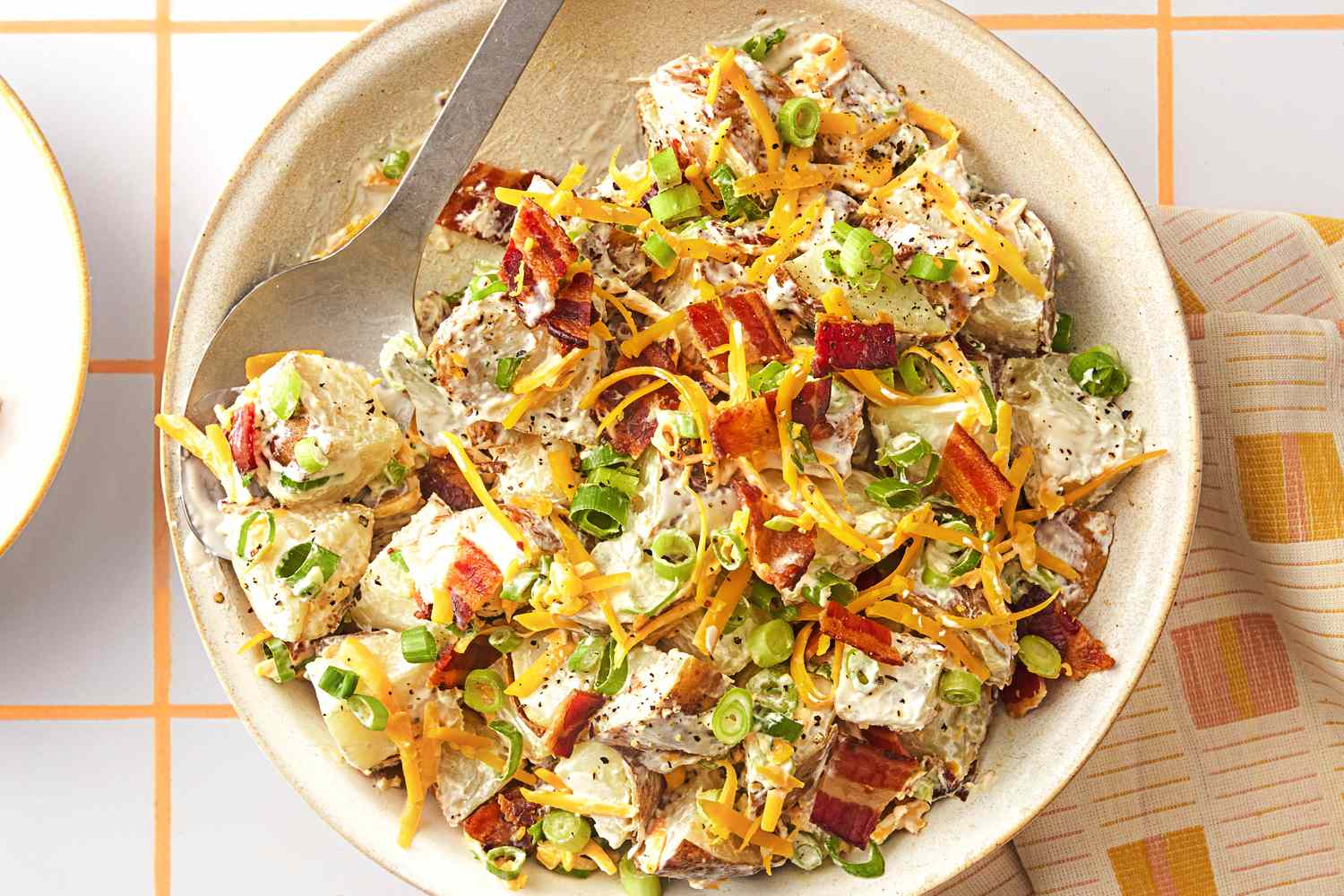 A bowl of loaded potato salad topped with bacon cheese and green onions