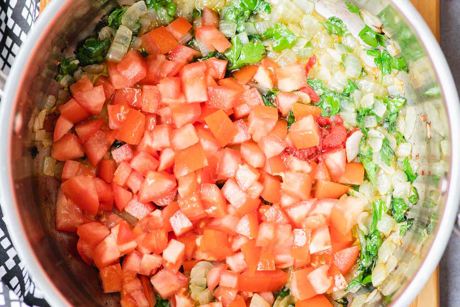 Adding chopped tomato and parsley to a pot to make a seafood stew.