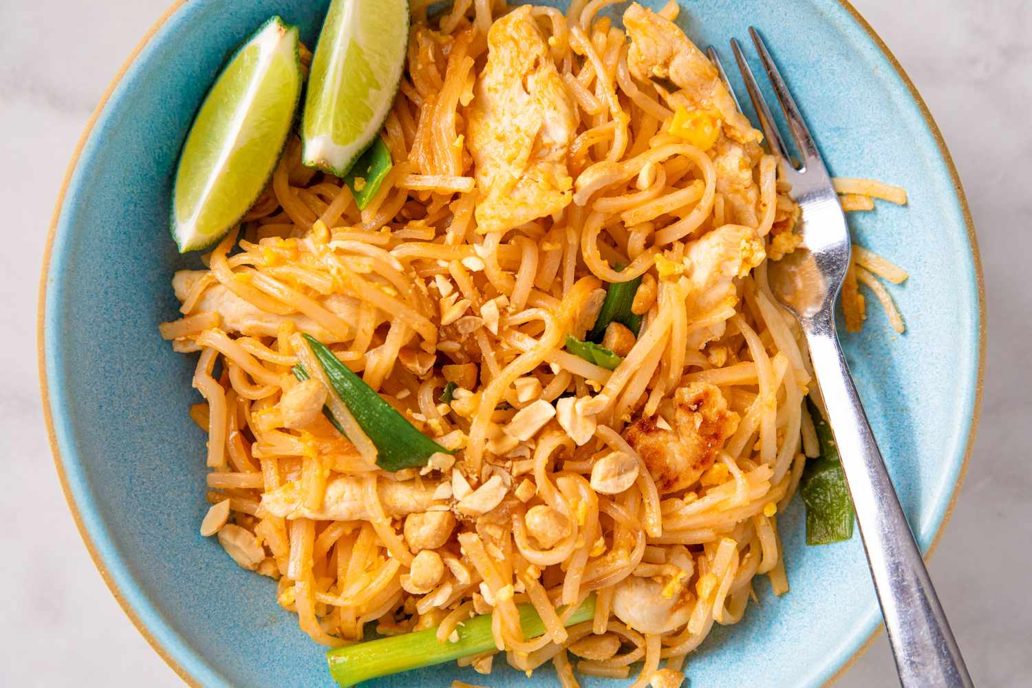 A bowl of pad Thai with lime wedges and a fork on the side