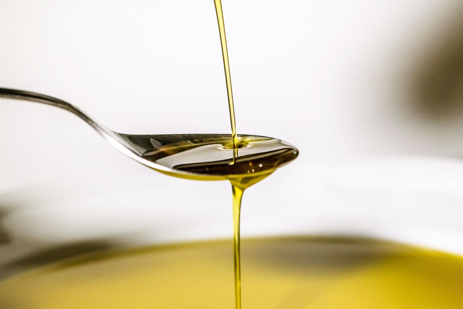 Olive oil being poured onto a spoon above a bowl