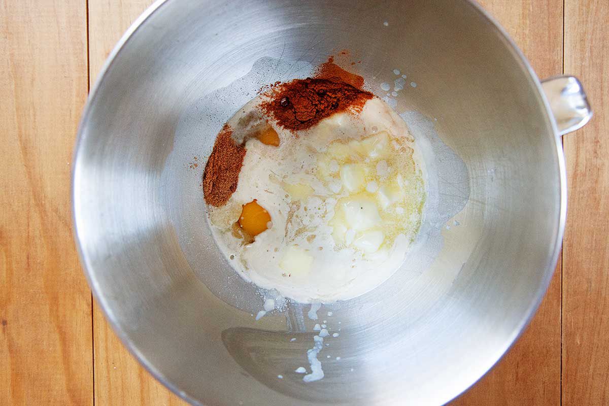 Melted butter, milk, yeast and spices are in a large bowl on a wooden table to make the best king cake.