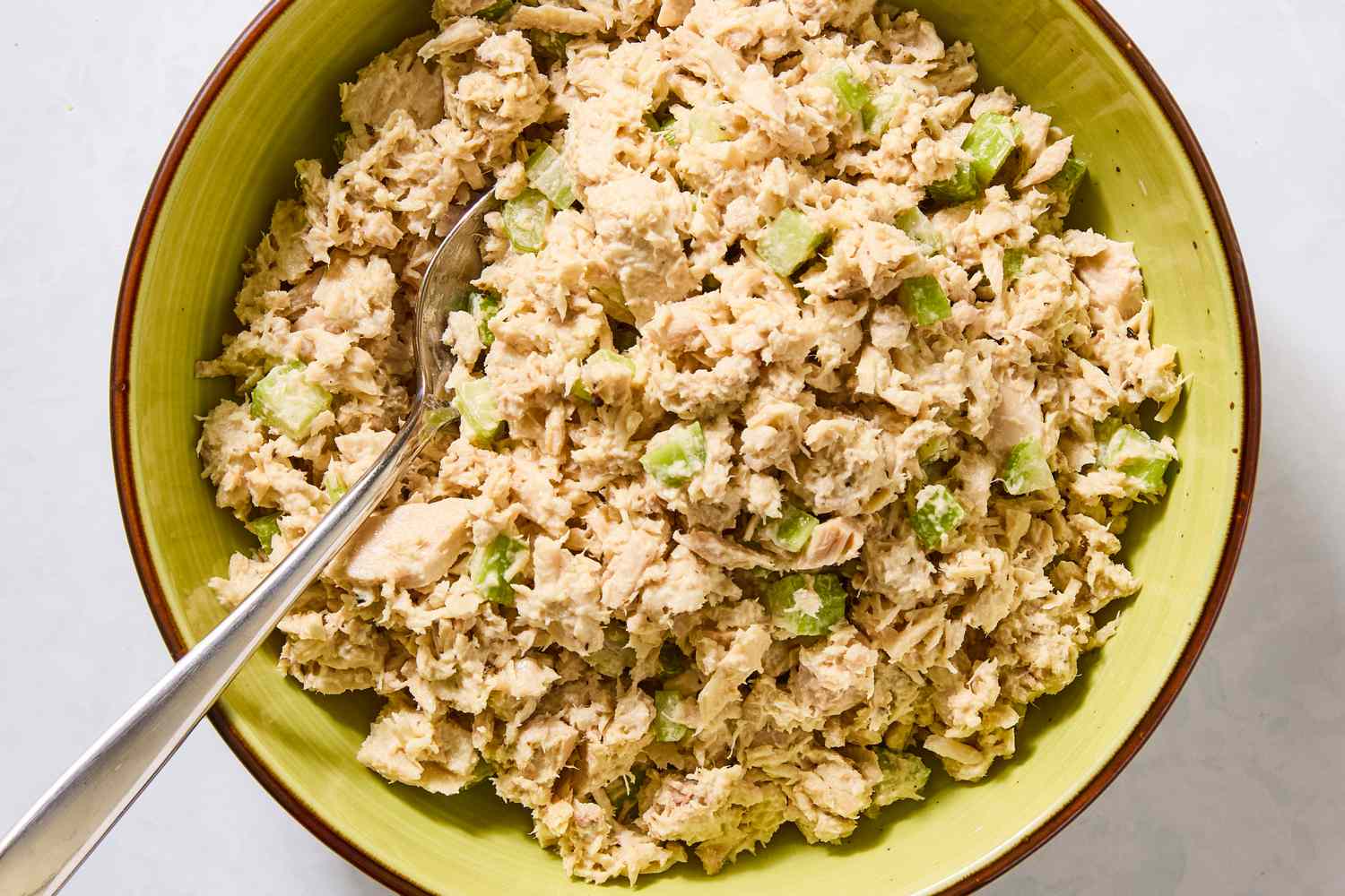 Tuna salad with celery in a bowl displayed with a spoon