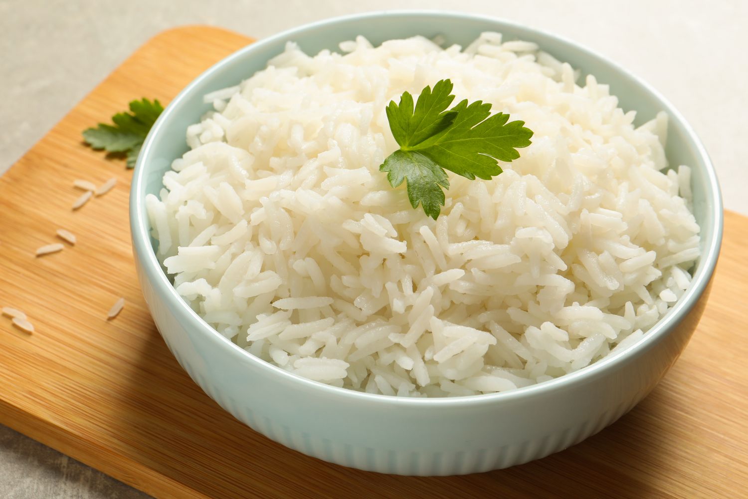 A bowl of cooked white rice garnished with parsley on a wooden surface