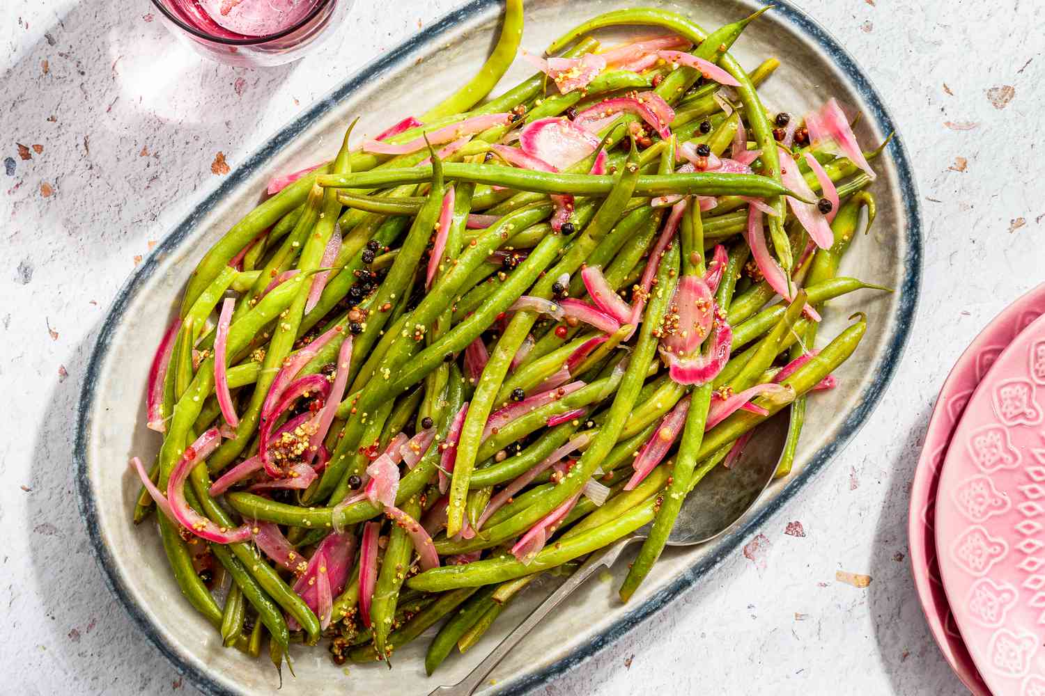pickled green beans on a platter next to a glass of water and a stack of plates
