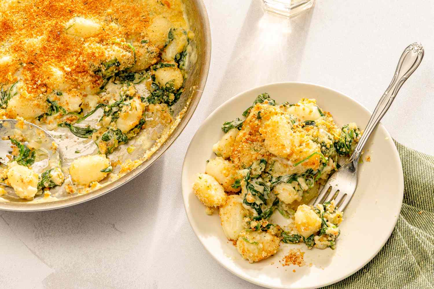 A dish of spinach and gnocchi baked with a crispy topping served on a plate with a fork