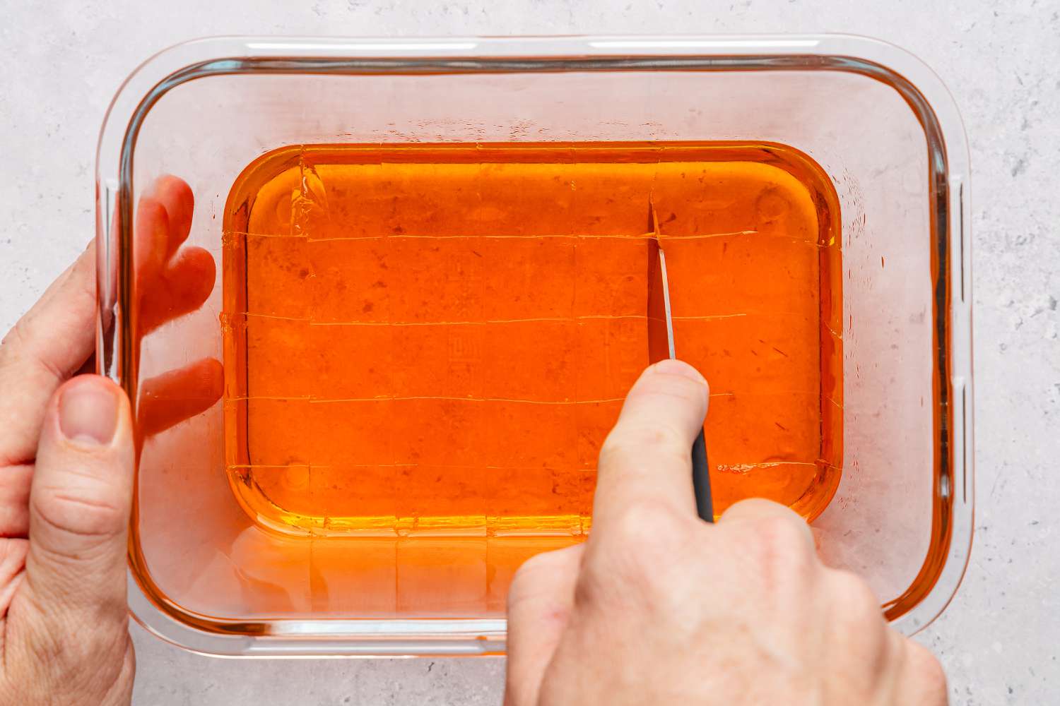 Overhead shot of a orange set jello getting cut into squares with a knife for the stained glass jello recipe