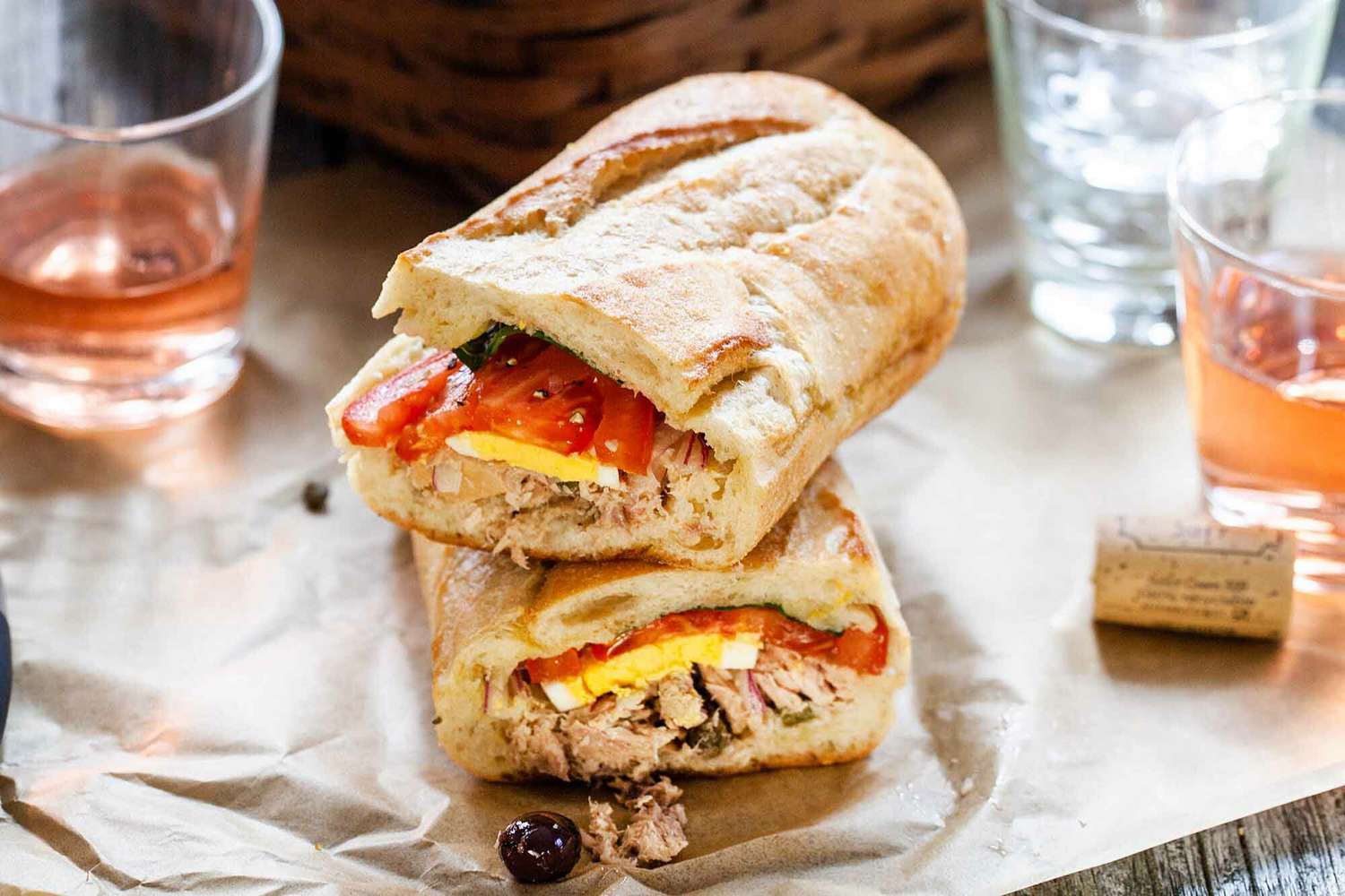 Pan Bagnat (French Tuna Sandwich) on Parchment Paper with Three Drinks Next to It