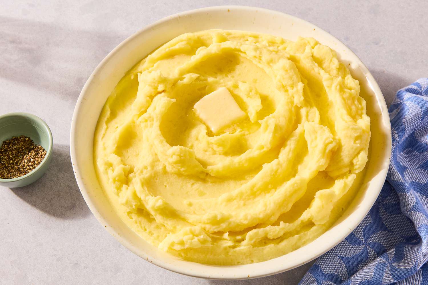 A bowl of golden mashed potatoes with a pat of butter melting on top