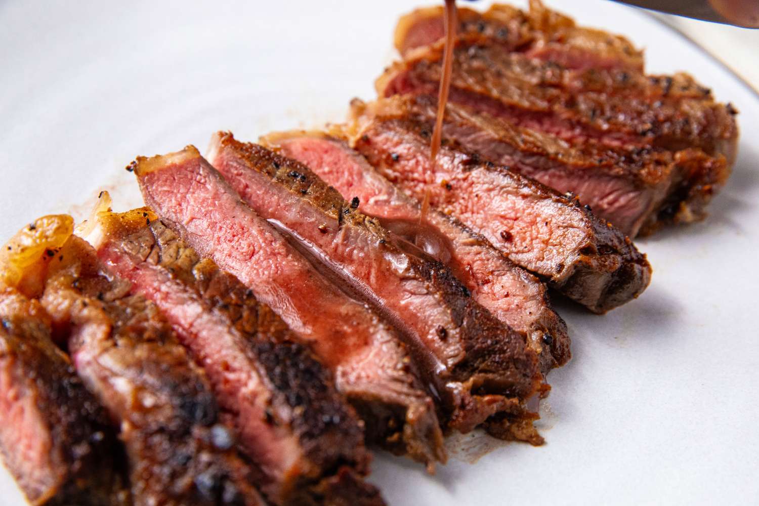 Sliced cooked steak with juices being poured over it
