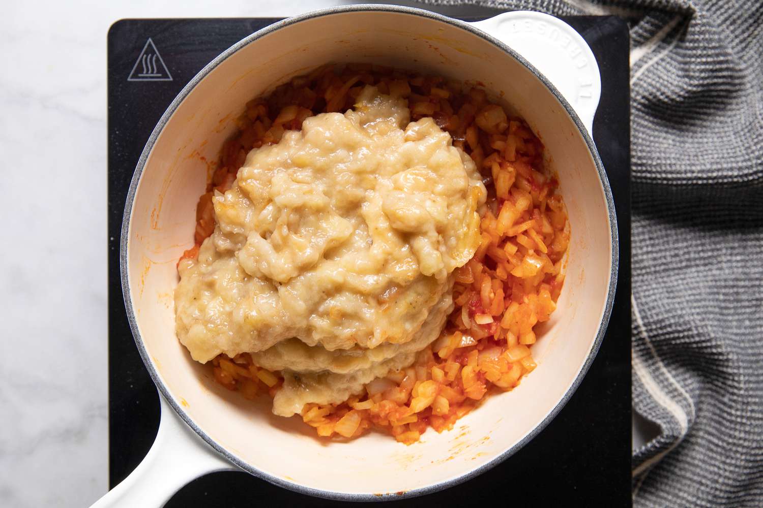 Mashed Bananas Added to Dutch Oven on a Portable Burner, and Next to It, a Grey Kitchen Towel for Banana Ketchup