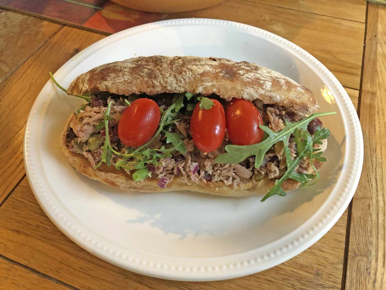 A sandwich on a plate containing tuna greens and cherry tomatoes