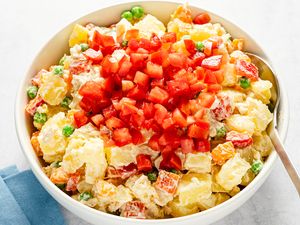 A bowl of potato salad with diced tomato garnish on top containing peas carrots and creamy dressing