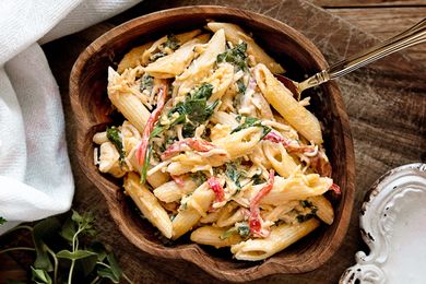 A bowl of pasta salad with vegetables and herbs on a wooden table