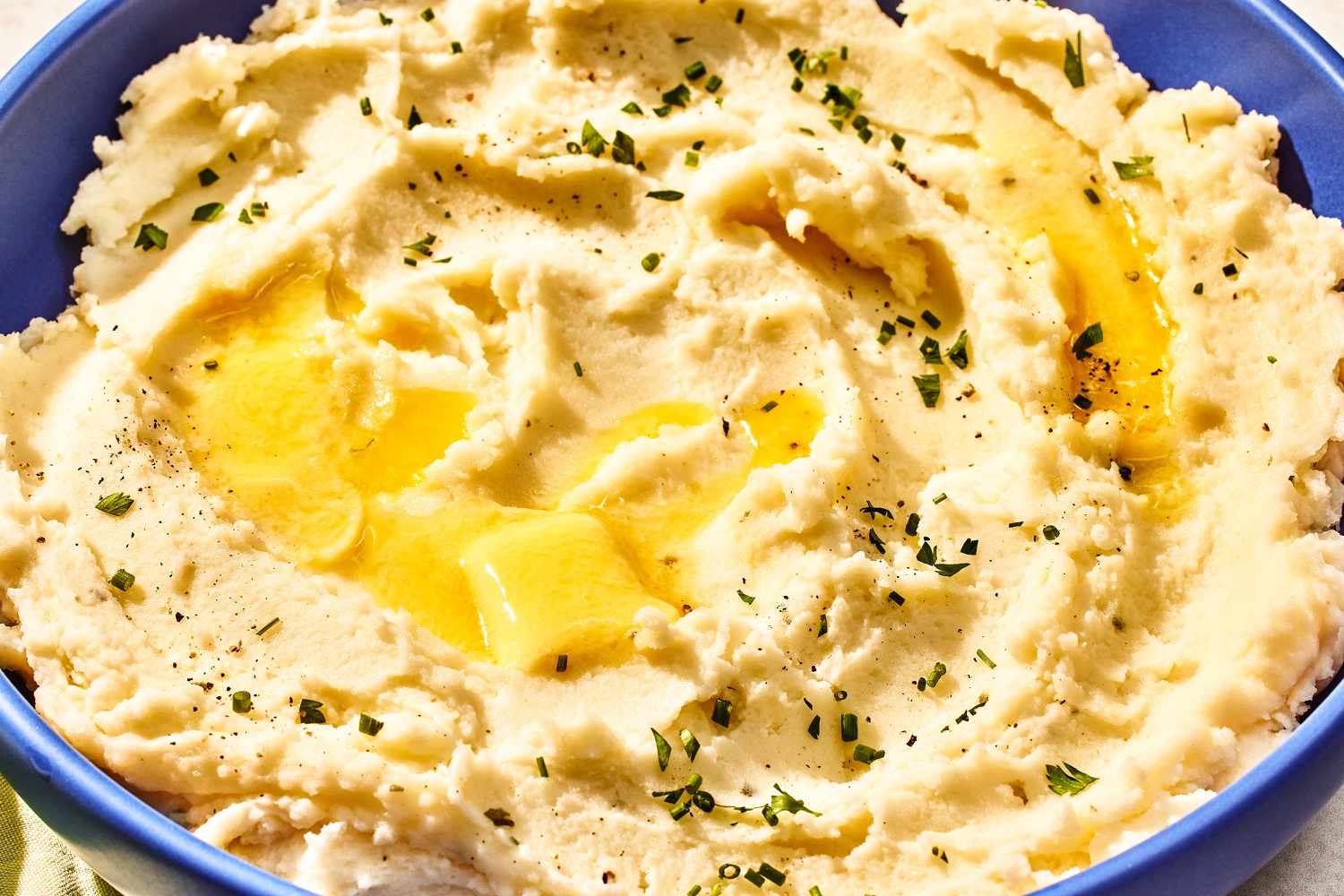 Overhead view of a large blue bowl of boursin mashed potatoes topped with herbs and butter