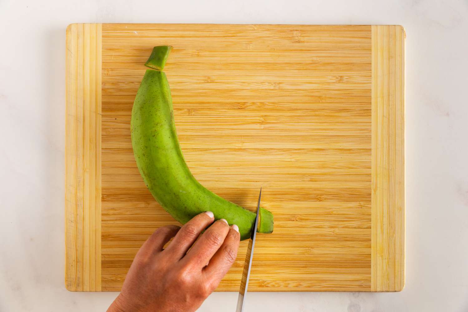 Ends of a Plantain Cut Using a Knife on a Cutting Board for Plantain Chip Recipe