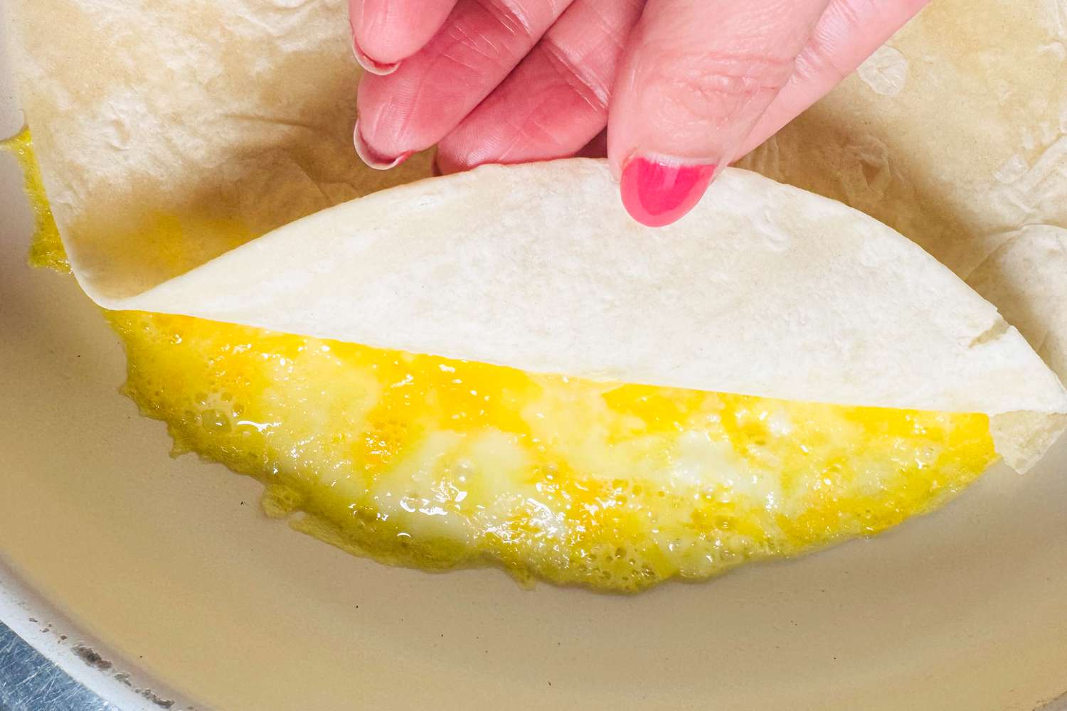Tortilla being folded over cooked eggs in a pan, hand visible adjusting the tortilla.
