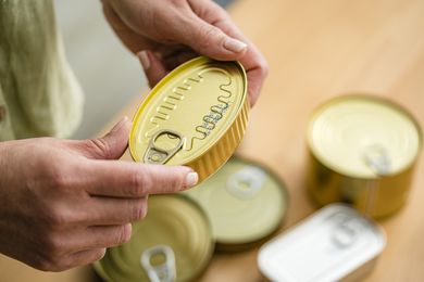 Person inspecting a sealed food can with other cans nearby on a wooden surface