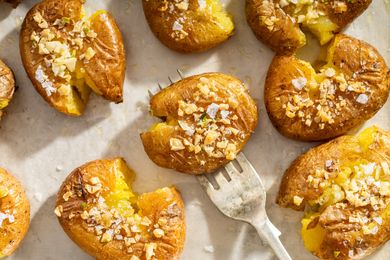 Roasted smashed potatoes topped with crushed nuts on a baking surface with a fork