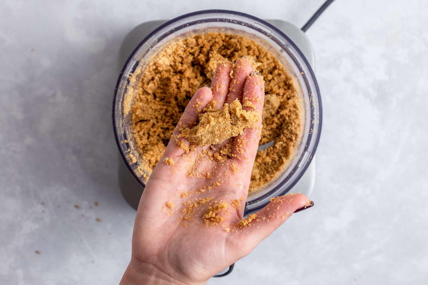 A hand squeezing the graham cracker mixture to make a no bake cheesecake recipe.