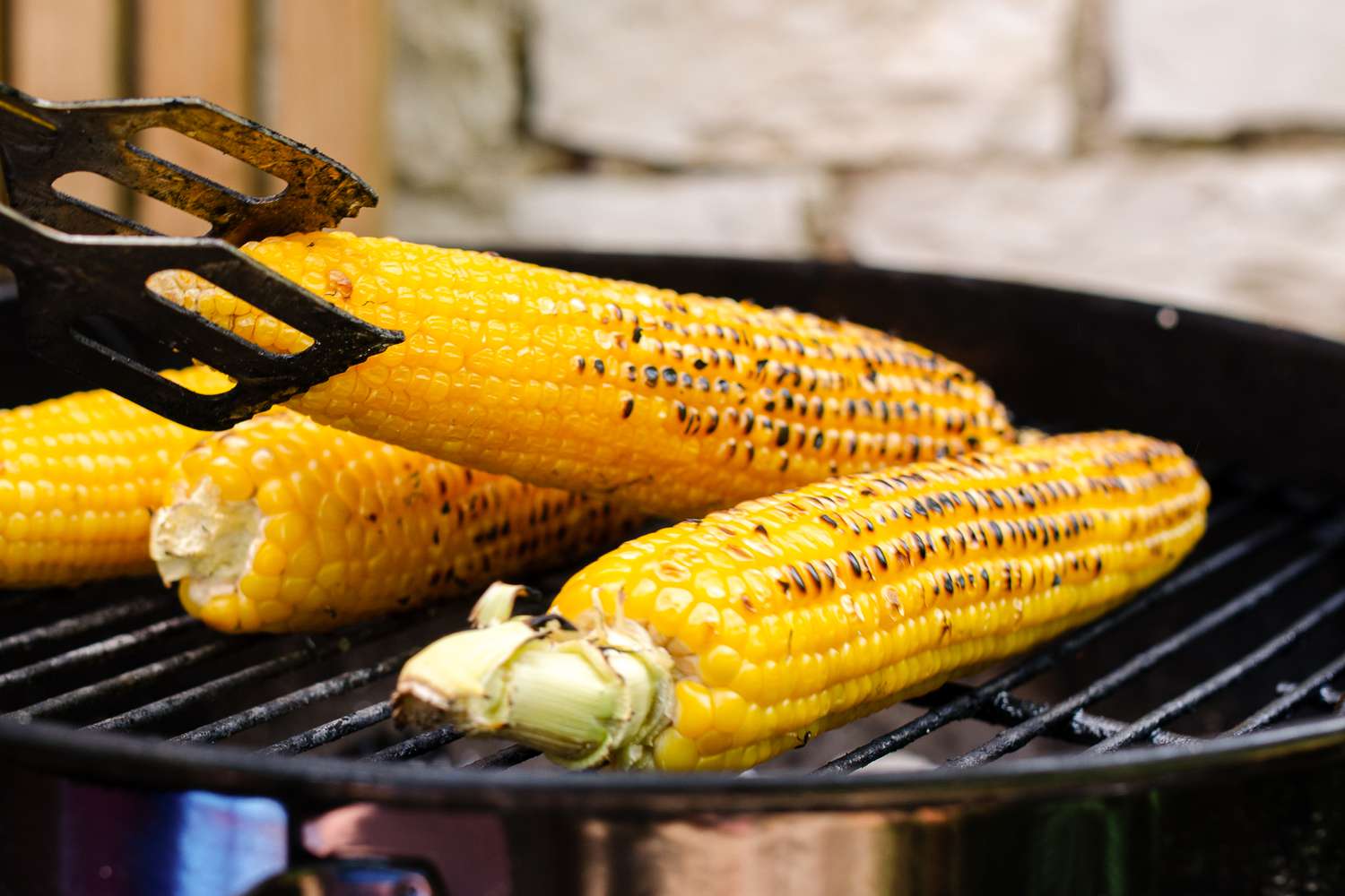 corn roasting on a grill with one turned using a pair of tongs